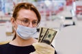 A red-haired girl in a medical mask stands with dollars in her hands near the store cash register Royalty Free Stock Photo