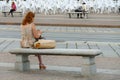 Red haired woman seated on a bench consulting her smartphone