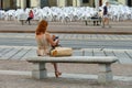 Red haired woman seated on a bench consulting her smartphone