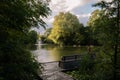 A red haired woman sitting alone on a bench in a calm relaxing park with pond during summer in Lund Sweden