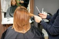 Red-haired woman sitting a front of the mirror and receiving haircut her red long hair by a female hairdresser in a hair Royalty Free Stock Photo