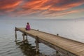 Red-haired woman sitting on a wooden dock watching the sunset