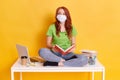 Red haired woman student on distance learning, working at home, young girl sitting on white table with crossed legs and holding Royalty Free Stock Photo