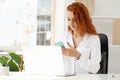 Red-Haired Woman Talking On Mobile Phone Working Remotely On Laptop Royalty Free Stock Photo