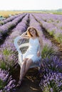 A red-haired woman in a white dress is sitting on a white chair in a field among the lavender.