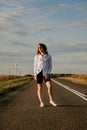 A red-haired woman in a white shirt walks along the road among the fields Royalty Free Stock Photo