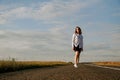 A red-haired woman in a white shirt walks along the road among the fields Royalty Free Stock Photo