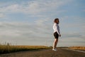 A red-haired woman in a white shirt walks along the road among the fields Royalty Free Stock Photo