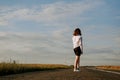 A red-haired woman in a white shirt walks along the road among the fields Royalty Free Stock Photo