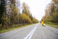 A red-haired woman in a yellow coat walks with a yellow suitcase along the highway in autumn. Royalty Free Stock Photo