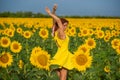 Red-haired woman in a yellow dress dancing with raised hands in a field of sunflowers. Beautiful girl in a skirt sun