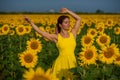 A red-haired woman in a yellow dress is standing in a field of sunflowers. Beautiful girl in a skirt sun enjoys a cloudless day in