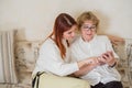 Red-haired woman teaches an elderly mother how to use a smartphone. Mother and adult daughter dressed in white blouses