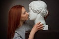 Red-haired young girl on a black background a gray t-shirt, kissing with a plaster bust Royalty Free Stock Photo