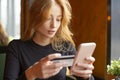 Red haired young woman making card payment through mobile phone to pay bills. Close up. Royalty Free Stock Photo