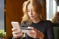 Red haired young woman making card payment through mobile phone to pay bills. Close up. Royalty Free Stock Photo