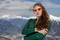 Red-haired young woman posing in green jumpsuit and glasses against the backdrop of snow-capped mountains, Austria Royalty Free Stock Photo