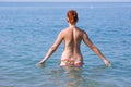 Red haired young woman in swimming trunks entering in sea