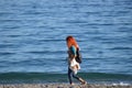 A red-haired young woman is walking on the beach of the mediterranean sea