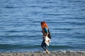 A red-haired young woman is walking on the beach of the mediterranean sea