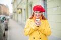 The red-haired young woman in a yellow coat and red beret is drinking coffee on the street to keep warm Royalty Free Stock Photo