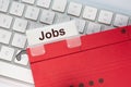 Red hanging folder on a keyboard has a tab with the word Jobs on it Royalty Free Stock Photo