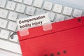 Red hanging folder on a keyboard has a tab with the words Compensation bodily injury on it Royalty Free Stock Photo