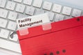 Red hanging folder on a keyboard has a tab with the words facility management on it