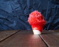 Red Hawaiian Shave ice, Shaved ice or snow cone dessert in a clear flower cup against a black background.