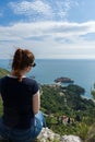 Red head girl hill enjoying Sveti Stefan island in Budva, Montenegro. Young woman looking to the adriatic sea and green cliff.