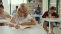 Red-head school boy wearing glasses sitting on the desk writing the dictation. Back to school learning. People and