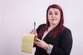 Red headed female wearing business suit taking notes on yellow notepad