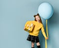 Teen kid in yellow sweatshirt, black skirt, knee-highs, boots. Kissing you, holding balloon, gift box, posing on blue background.