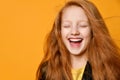 Red-headed teenage child in black jacket and yellow t-shirt. She laughing with closed eyes, posing on orange background. Close up