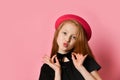 Red-headed teenager in black dress and red hat. She kissing you, holding on to choker, posing on pink studio background. Close up Royalty Free Stock Photo