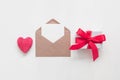Red heart, blank card mockup in craft envelope and gift box in a row on white painted background. Valentine`s Day. Top view, flat