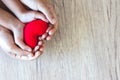 Red heart in child hands and parent hands on wooden table background Royalty Free Stock Photo