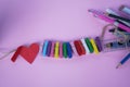 Red heart with colorful wooden clips on rope and pencil pens on soft pink and purple background. Creative concept Royalty Free Stock Photo