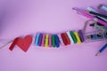 Red heart with colorful wooden clips on rope and pencil pens on soft pink and purple background. Copy space. Creative concept Royalty Free Stock Photo