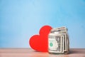 Red heart and donation jar with money on table against color background.