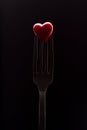 Red heart on fork, black background.
