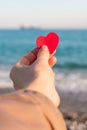 Red heart in the girl`s hand against the background of the sea horizon.