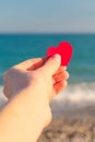 Red heart in the girl`s hand against the background of the sea horizon.