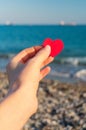 Red heart in the girl`s hand against the background of the sea horizon.