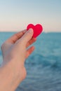 Red heart in the girl`s hand against the background of the sea horizon.