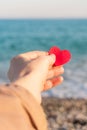 Red heart in the girl`s hand against the background of the sea horizon.