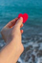 Red heart in the girl`s hand against the background of the sea horizon.