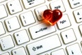A red heart lies on a white keyboard for a computer next to the enter key close-up. The concept of likes for social networks,