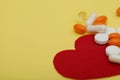 Red heart and a lot of bright pills of drugs on a yellow background.