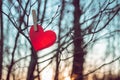 Red heart made of paper hangs on clothespin on tree branch on backdrop of sunset sky